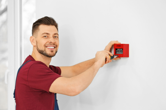 Técnico instalando acionador manual, um dos componentes do sistema de detecção de incêndio.