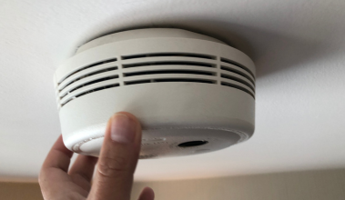 Detector de fumaça instalado no teto passando por verificação durante manutenção do sistema de alarme de incêndio.